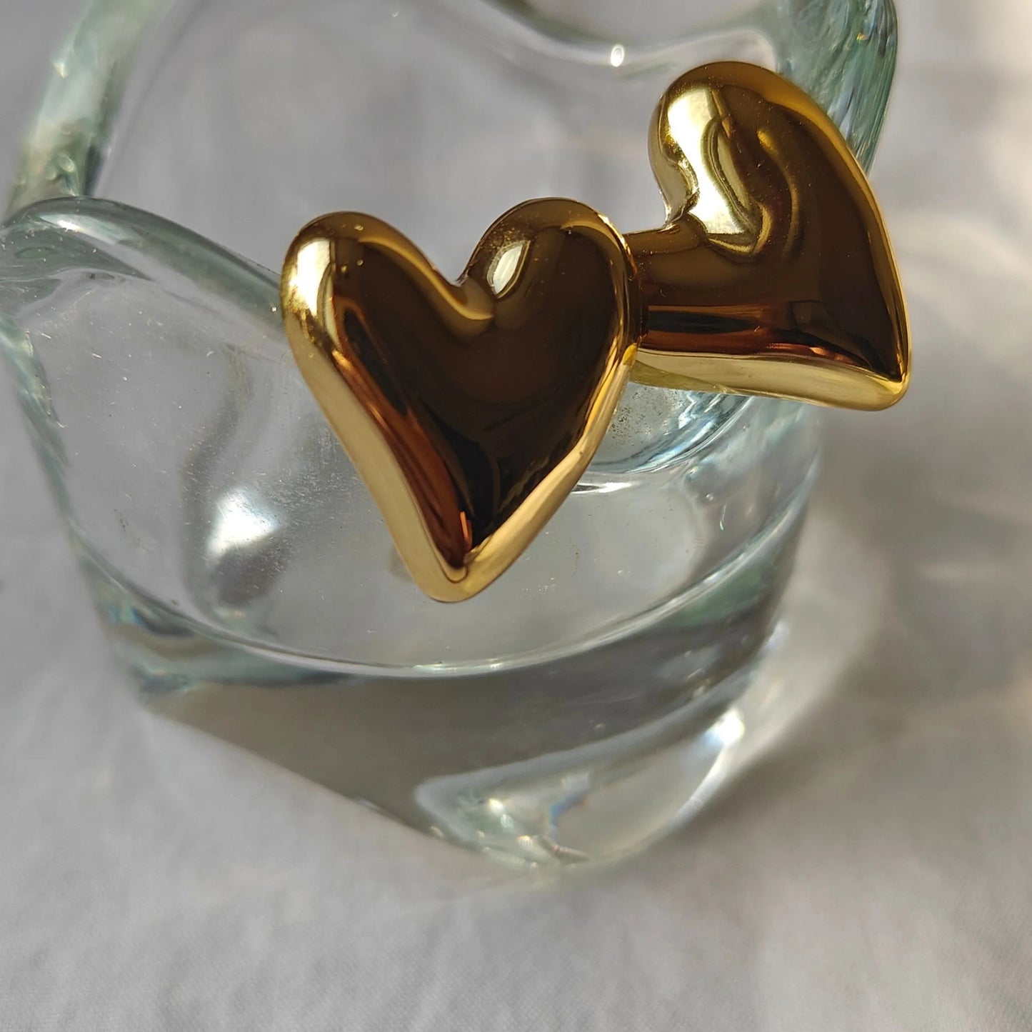 Gold Tone Heart Melt Stud Earrings resting on a small glass tea-lite candle holder